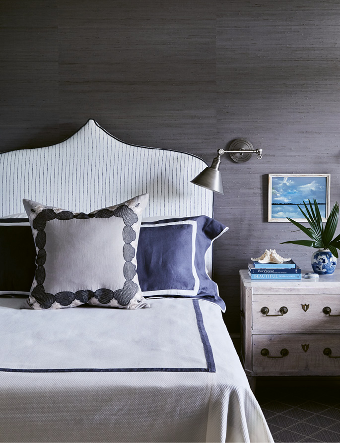 The guest bedroom’s steely grey-blue grasscloth-covered walls allude to the creek at night. A headboard covered in a Christopher Farr indigo-striped linen, duvet by Leontine Linens, and 19th-century nightstand from Parc Monceau Antiques in Atlanta complete the space.