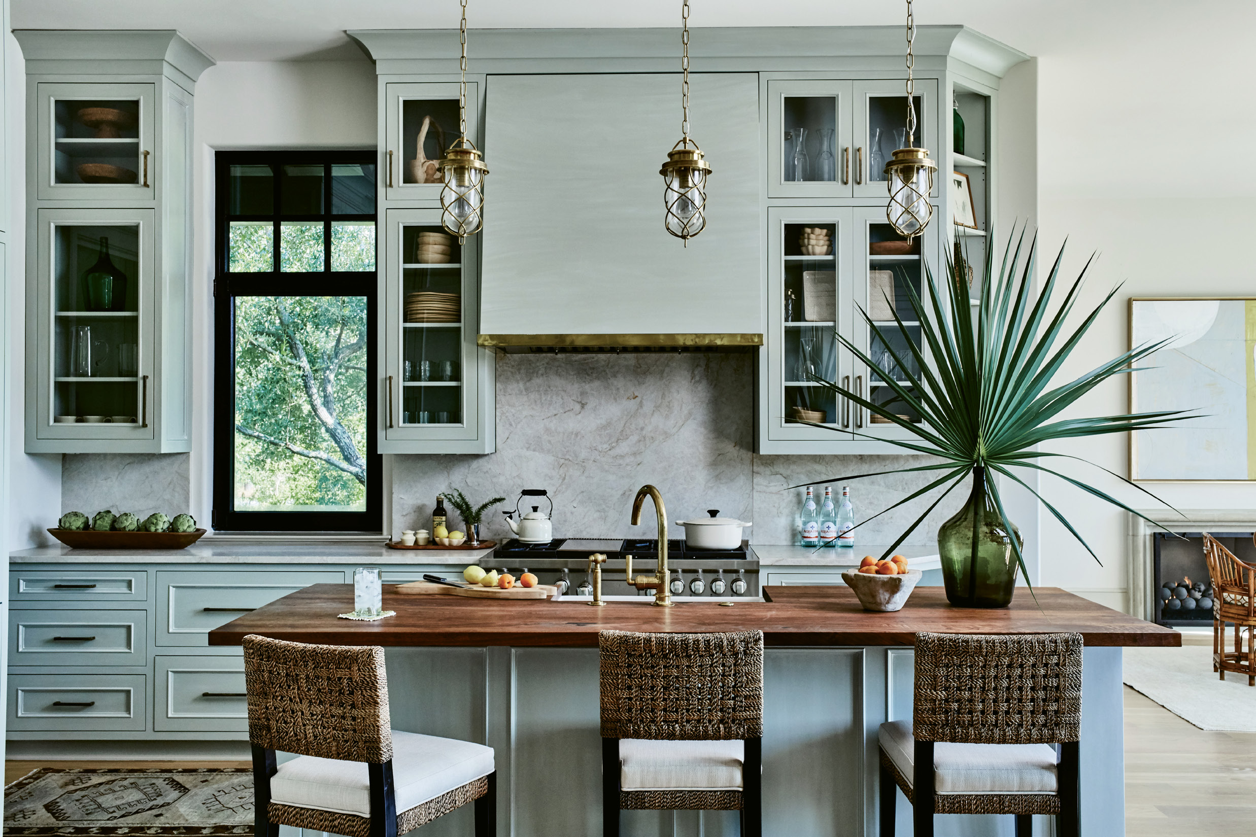WARM &amp; INVITING: Brass accents—the faucet, pendant lighting, and custom trim around the hood—continue in the kitchen. “It complements the soft sage-green cabinetry and warms up the space,” says interior designer Charlotte Lucas. She chose quartzite for the countertops and backsplash for its hue and durability and walnut to top the island for additional warmth and interest.