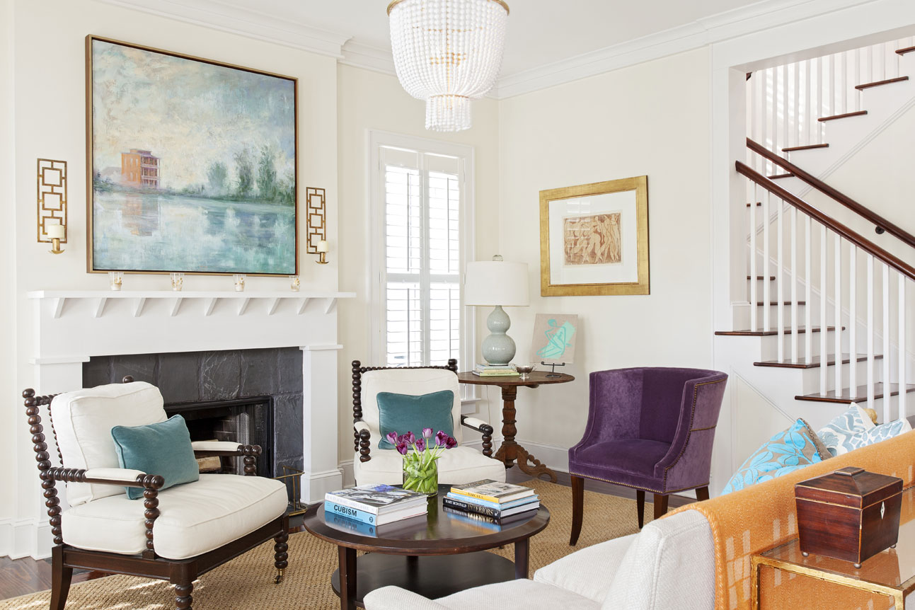 In the living room, a woven rug, creamy white walls, and neutral upholstered pieces contrast nicely with an orange throw, a violet velvet chair, and a blue-hued Linda Fantuzzo painting depicting I’On a decade ago.