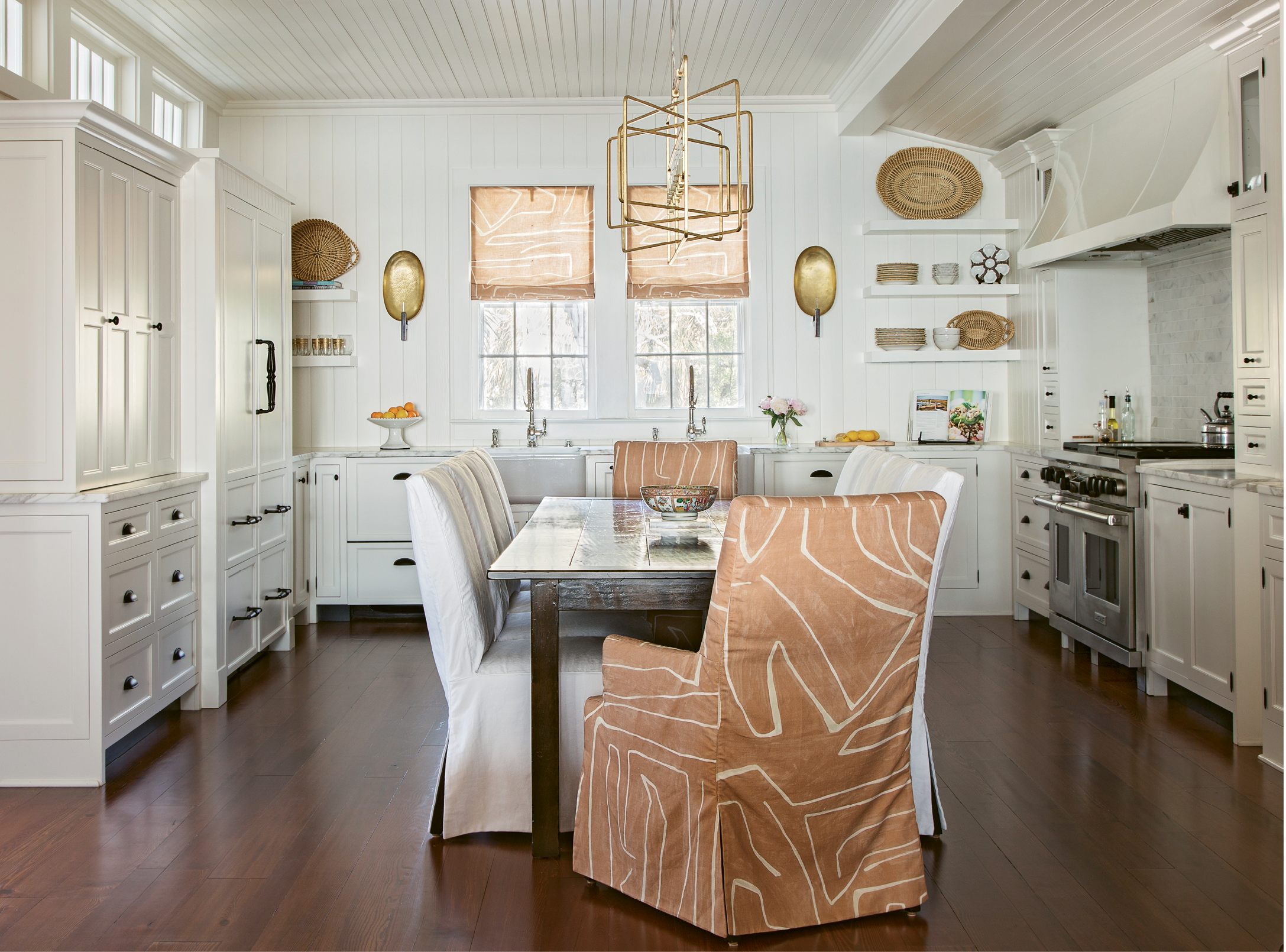 GOLDEN TOUCH: In the kitchen, simple roman shades in an abstract Kelly Wearstler fabric and clean-lined open shelving are offset by dramatic hammered-gold sconces. Instead of an island, the room is anchored by a custom dining table and comfy slip-covered chairs.