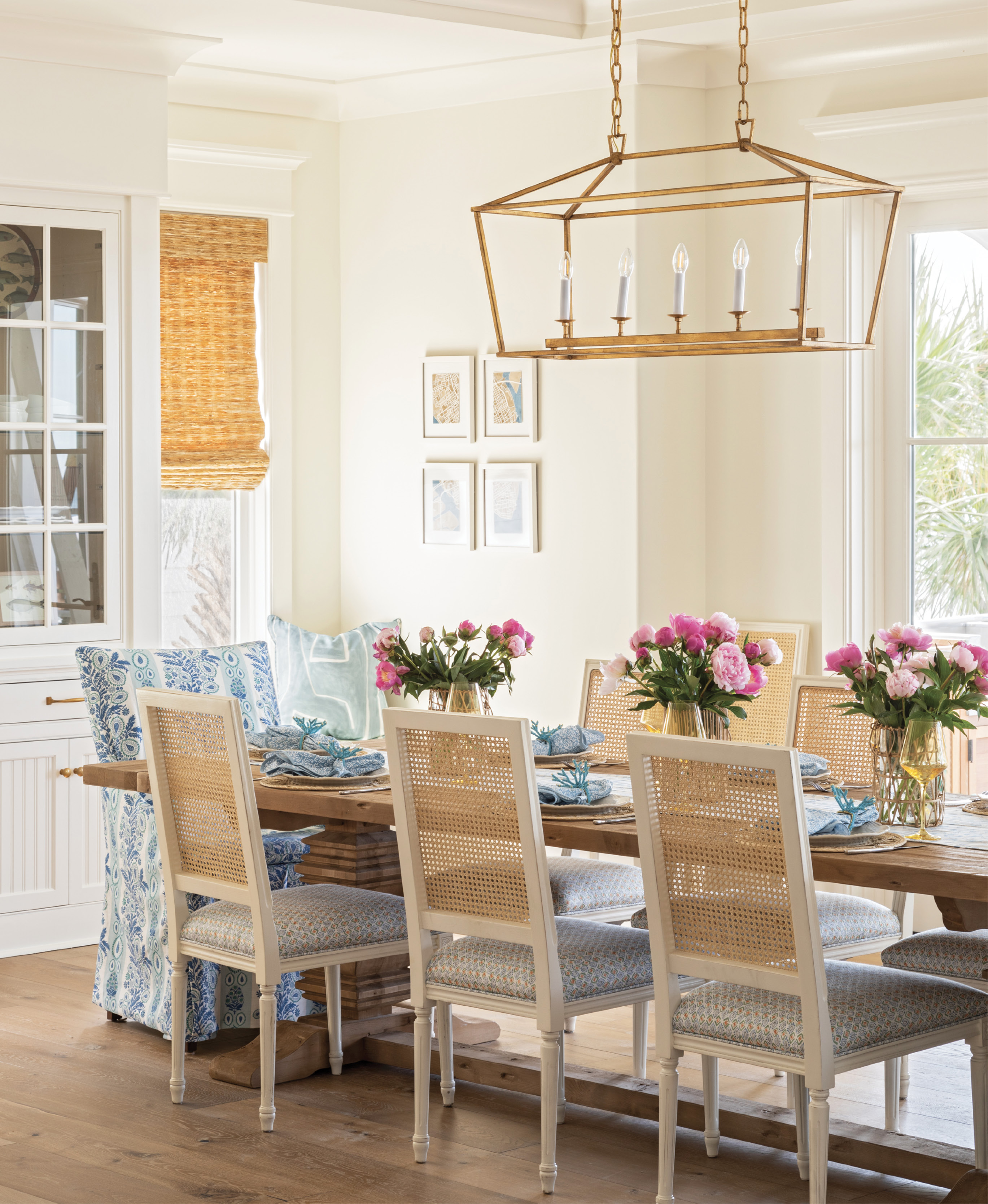 GOOD VIBES: In the dining area, windows were replaced with French doors, flooding the space with natural light and making a more direct thoroughfare to the outdoor kitchen. A fun suite of fabrics—by Rebecca Atwood (cane-back chair seats), Charlotte Gaisford (slipcovered host chairs), and Kelly Wearstler (window seat pillow)—energize the space, which centers around a sweeping Restoration Hardware trestle table.