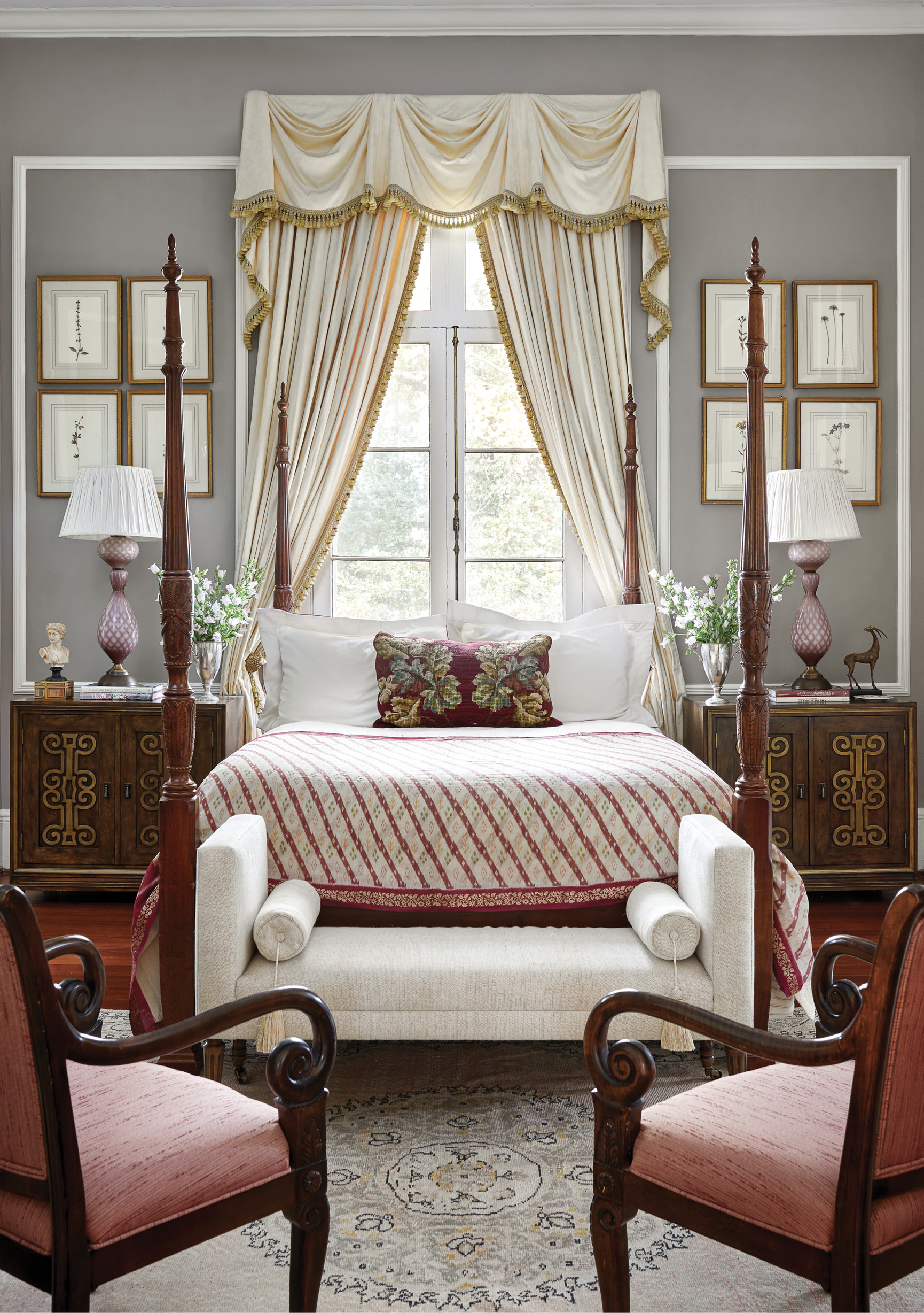 Color Story: In the primary bedroom, Ralph reused much of the Fergusons’ existing furniture, refreshing the space with a new palette of creams, purples, and burgundies. A vintage textile rug and custom shams add interest to the four-poster bed, and a custom bench is covered with a durable Itex fabric to accommodate the couple’s two dogs. Vintage Murano glass table lamps highlight their collection of botanical art, accentuated by the Benjamin Moore “Elephant Gray” wall paint.
