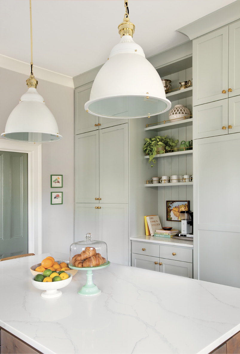 The space between: A coffee nook with slim, brass-accented shelves hung on a shiplap-covered wall breaks up the expansive floor-to-ceiling pantry that also houses a full fridge and freezer behind its Benjamin Moore “Gray Wisp”-painted cabinets. Pulls from Water Street Brass complement the shelves and the oversized Restoration Hardware pendants hanging over the quartzite-topped island.