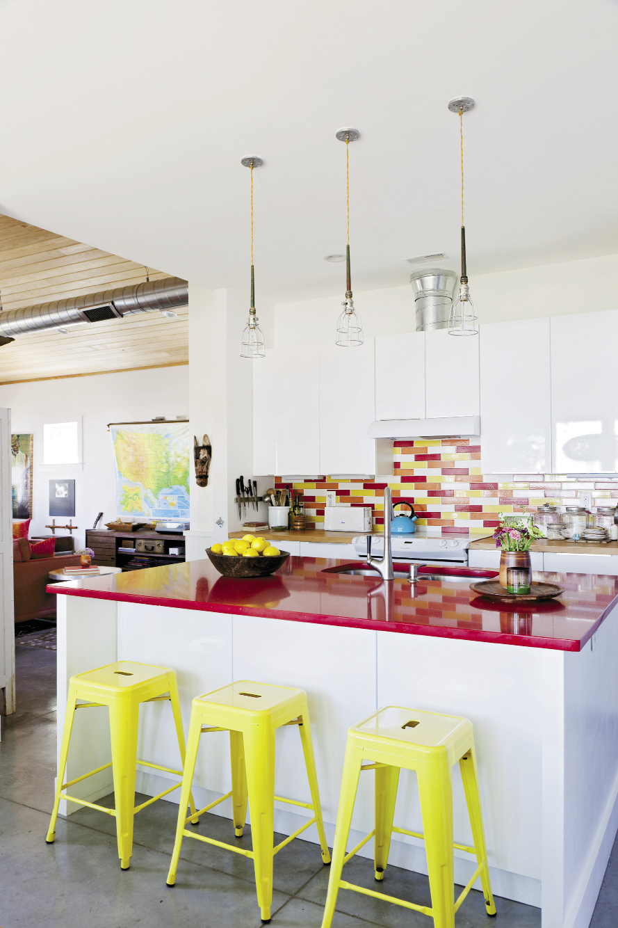 Yellow aluminum stools, a sparkly red quartz counter top, and a vibrant tile backsplash add doses of color to the kitchen.