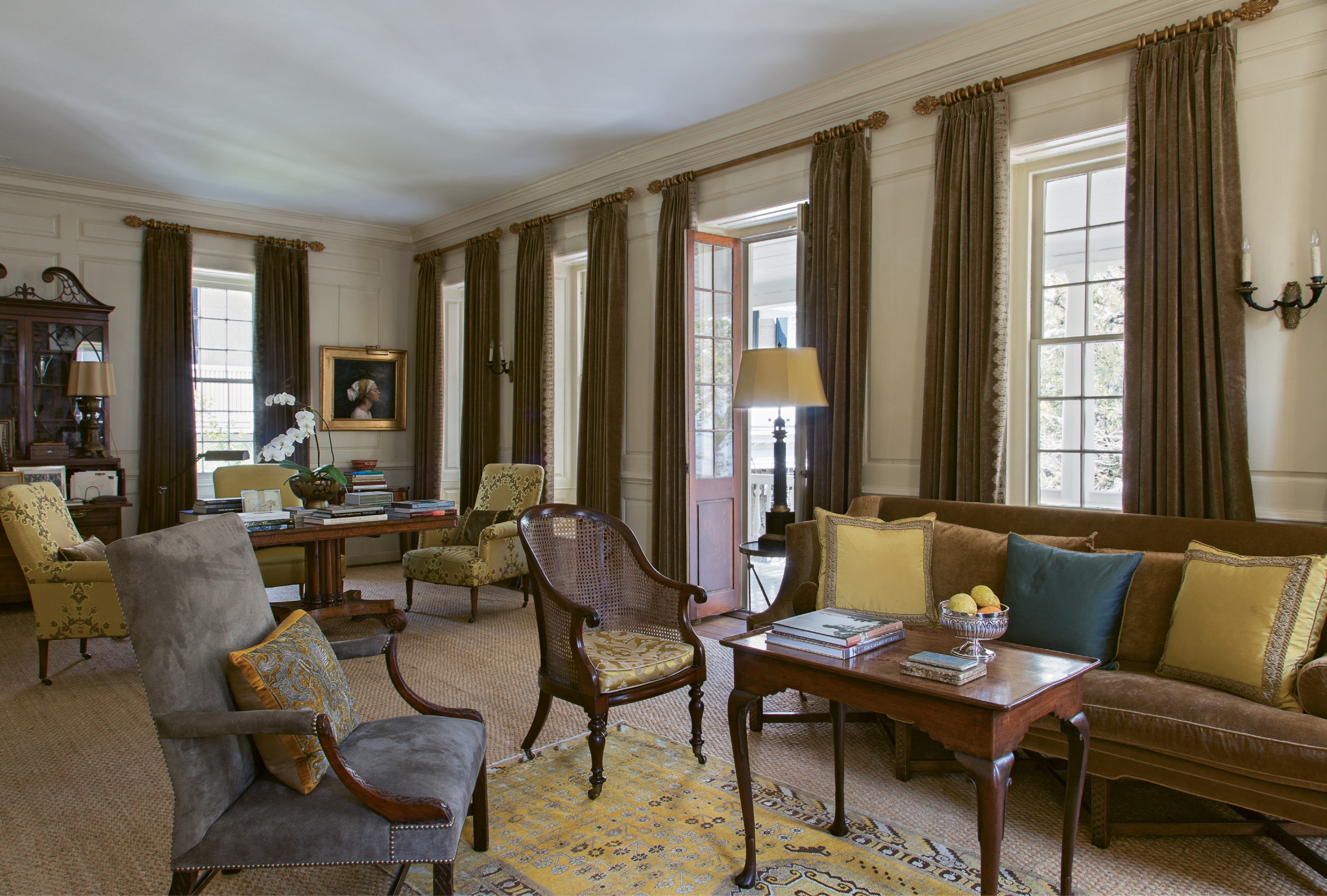 The upstairs drawing room is outfitted in a sophisticated palette of rich browns and yellows. An inviting mix of textures, from an antique Khotan rug atop seagrass to suede upholstery on the 18th-century armchair, adds visual interest.