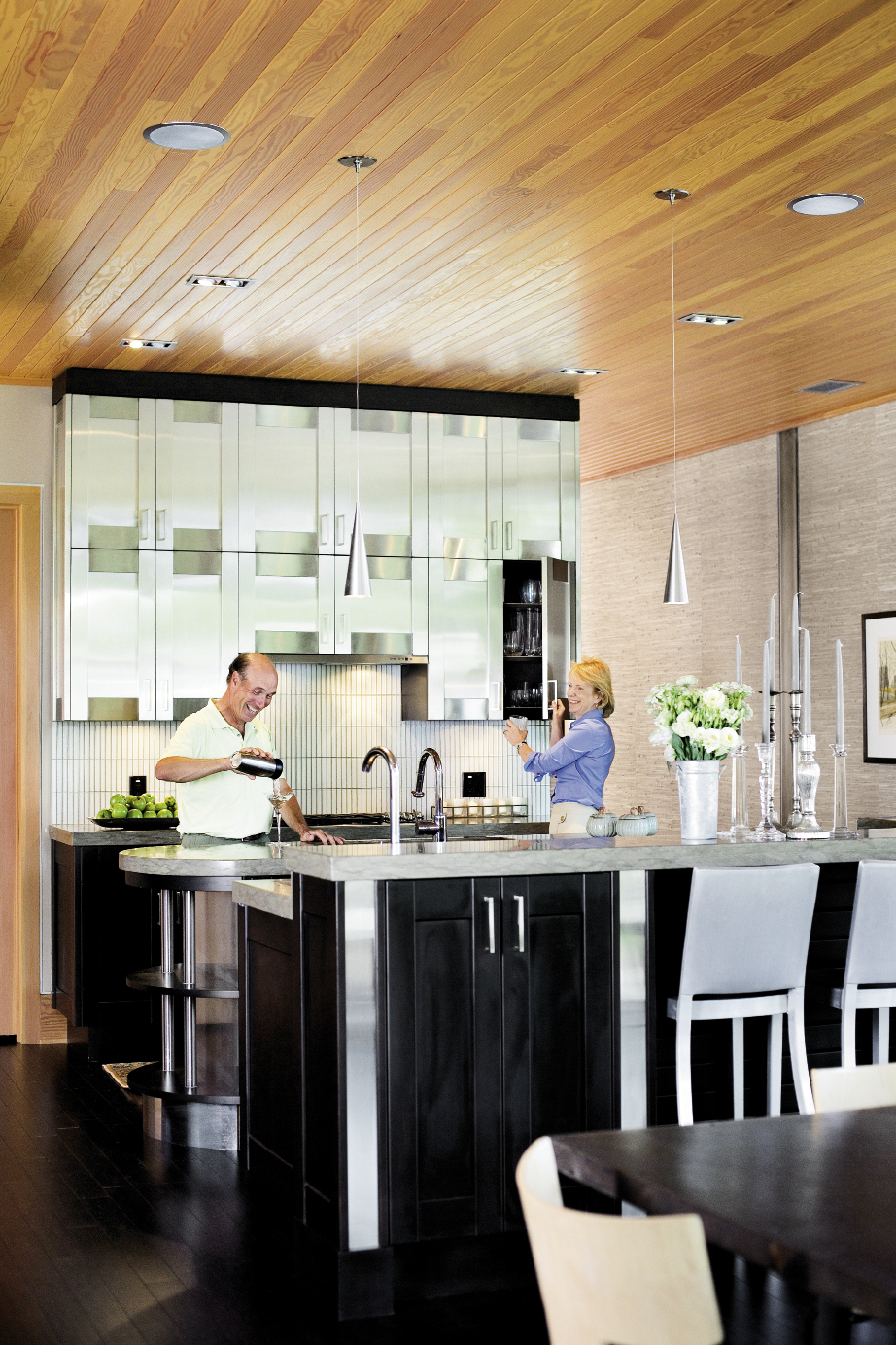 the pair in their open kitchen, anchored by stainless steel upper cabinetry.