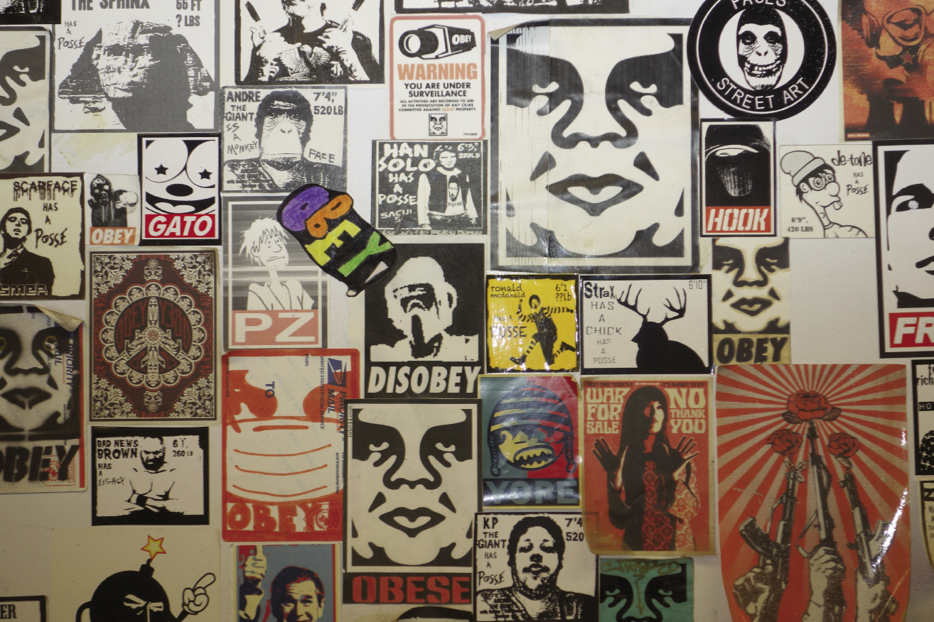 and a close-up of sticker graffiti in a public bathroom, including Fairey’s “Obey Giant.”