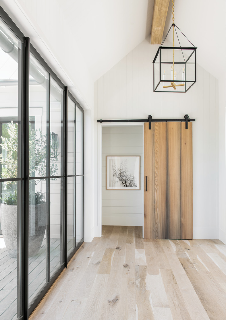 Feature &amp; Function: Designed to draw the eye to the landscape beyond its floor-to-ceiling windows, the entryway’s white oak flooring, cypress barn door, and wooden beam are accented by steel and glass, including an Urban Electric light fixture and custom door hardware.
