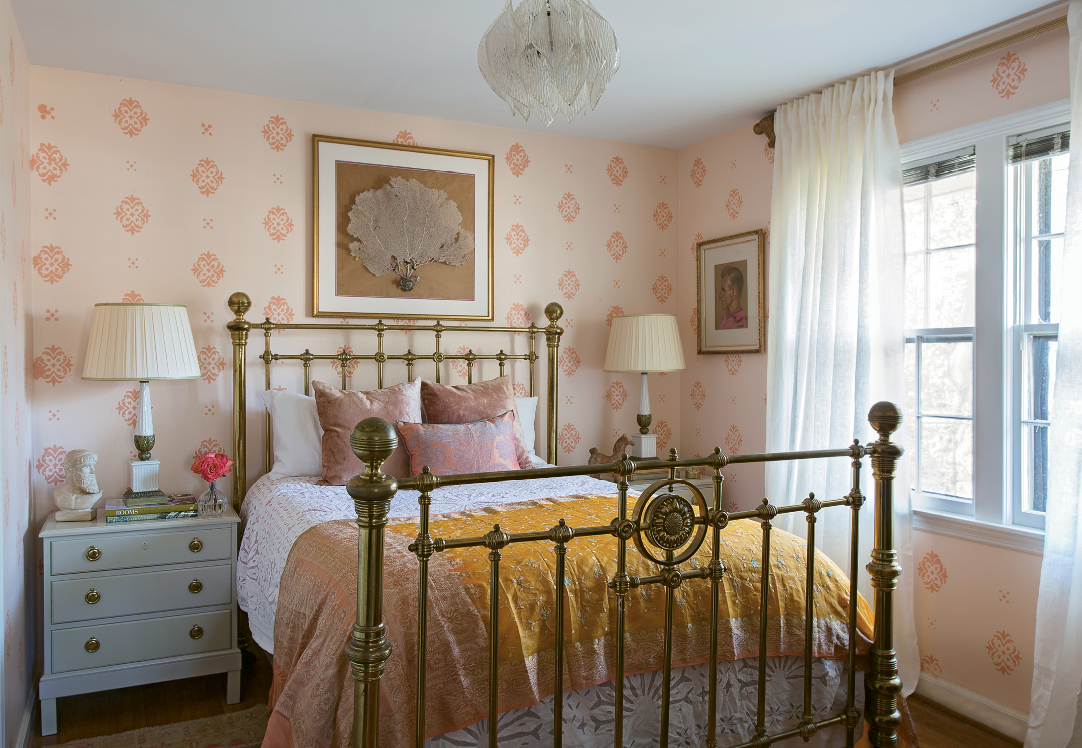 PRETTY IN PINK: In Tinkler’s bedroom, a pink-on-pink hand-stenciled motif is more affordable (but no less stunning) than wallpaper. Tall brass bedside lamps and a clear acrylic light fixture help the eight-foot ceilings seem higher.