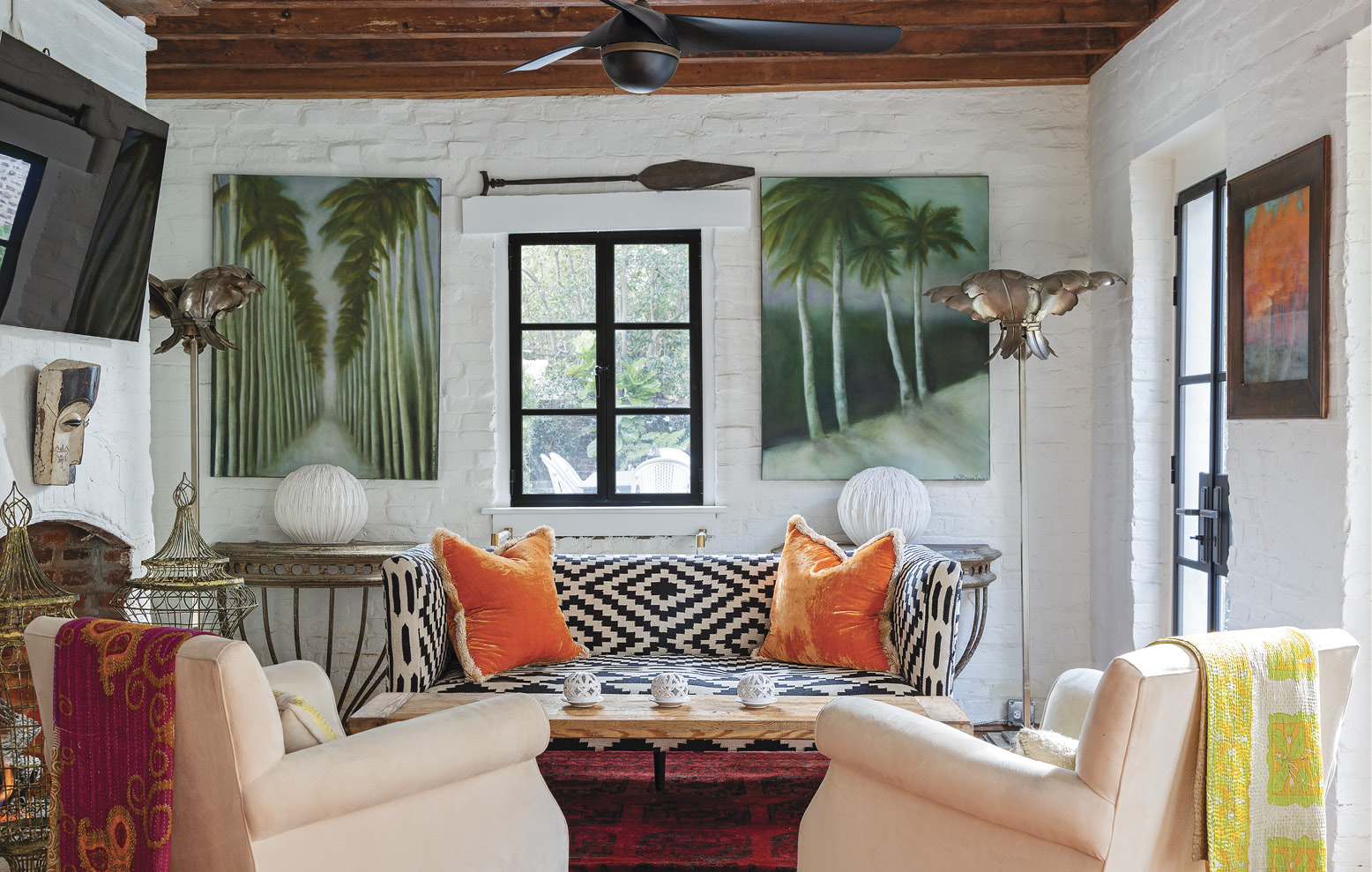 The former kitchen house is now a charming guest suite—and Betsy’s favorite space to watch the morning news. A kilim-upholstered sofa with orange velvet pillows from Fritz Porter lends a Middle Eastern vibe to the cozy cottage, while palm trees painted by Betsy mimic the vintage floor lamps.