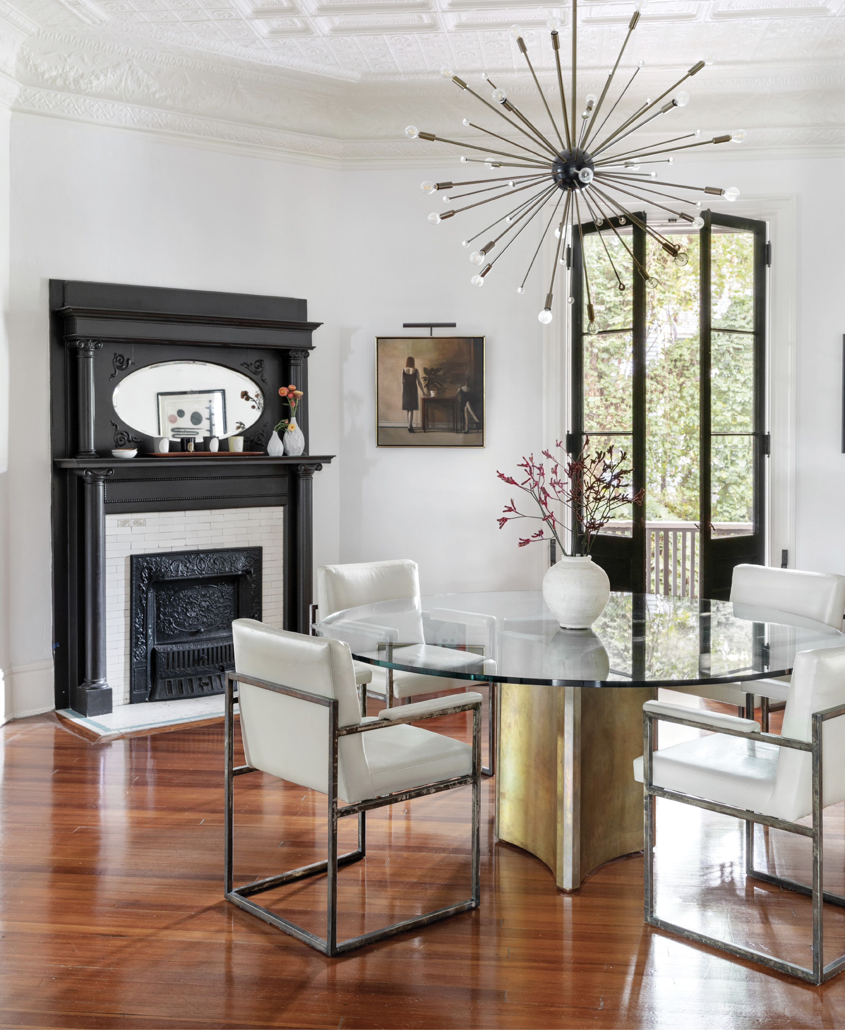Statement Pieces: In the dining room, the clean modern lines of the brass and metal table and vintage Mastercraft metal-frame chairs mesh with historical features, including the original fireplace and quarter-sawn pine floors. The stark white walls help draw the focus to the ornate ceiling and large “Imogene” chandelier from Arteriors Home.