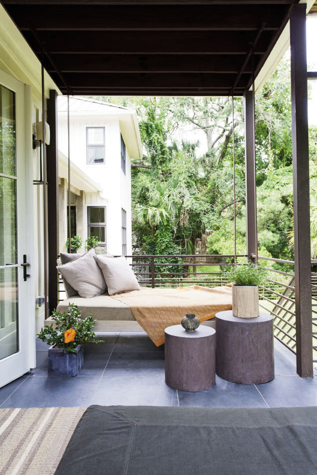 A daybed is suspended from a corner of the kitchen porch and overlooks the grassy backyard.