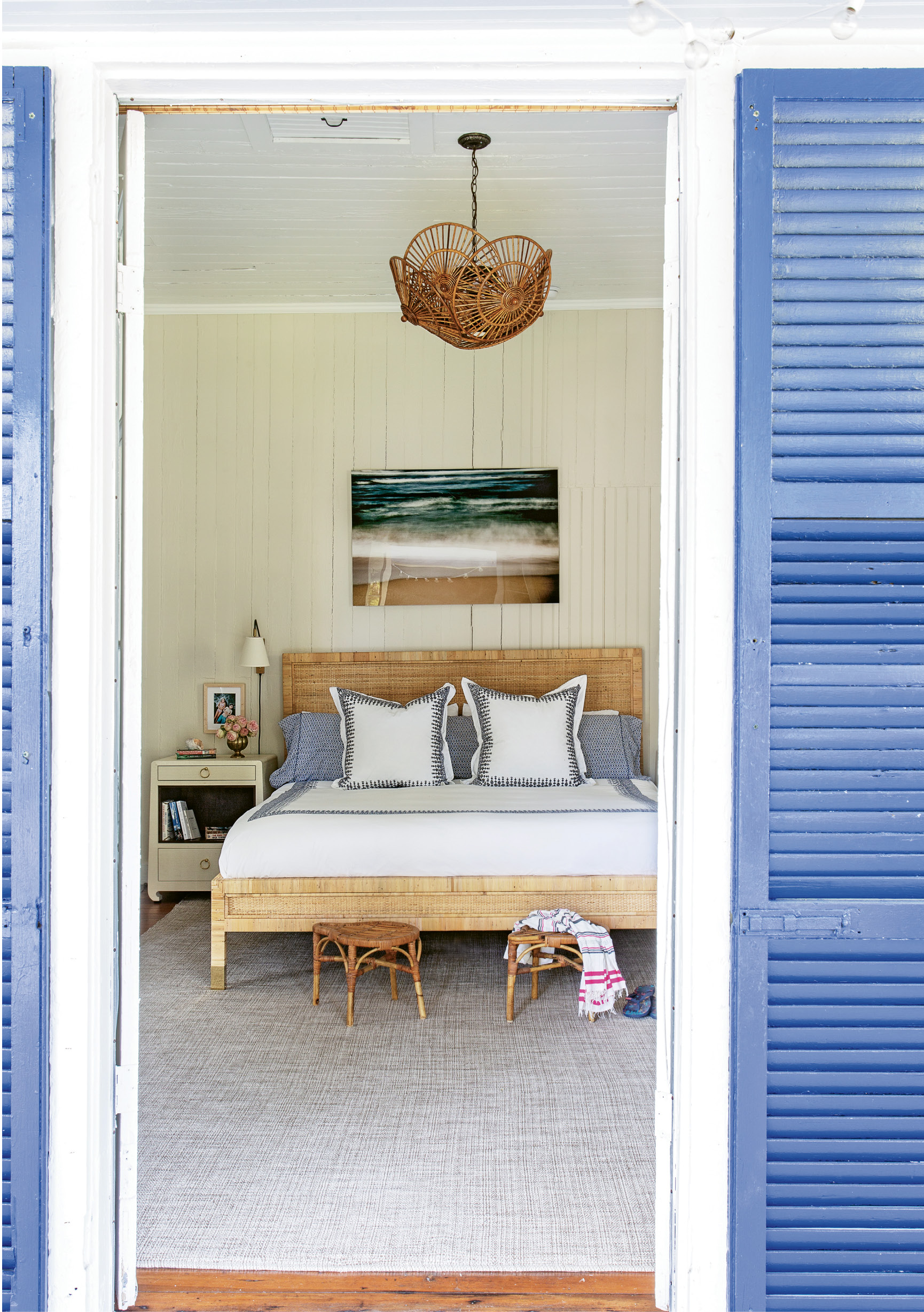 Comfortable Quarters: A large Dash and Albert rug softens the master bedroom, which has its own access to the porch. Two vintage rattan stools provide the perfect spot to drop the towels post-beach day, and a pair of Bungalow 5 bedside tables are the ideal place to stash summer reading.