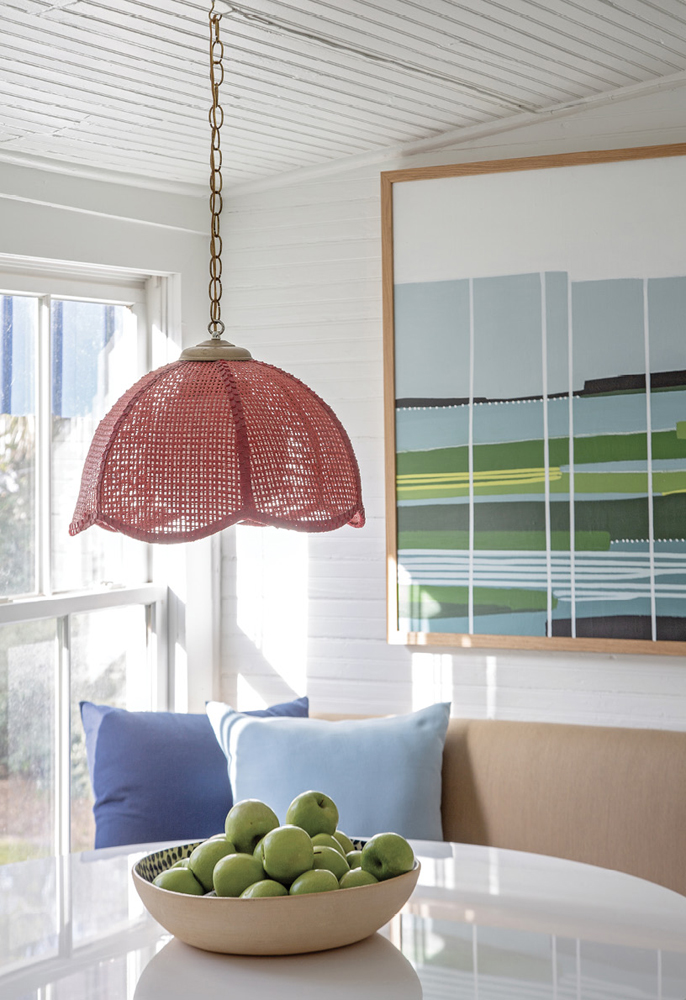 A vintage red wicker pendant light in the breakfast nook is one of the homeowner’s favorite finds. A painting by Isle of Palms-based artist Cindy DeAntonio presides over the scene.