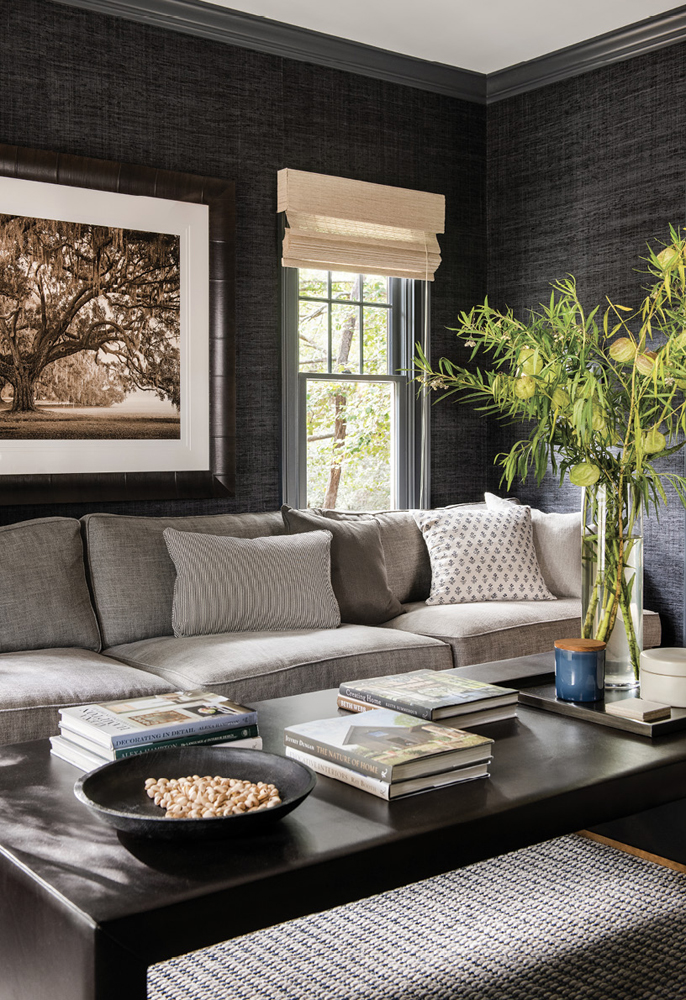 The couple added a wall to create a cozy space for watching television and enhanced it with a dramatic Phillip Jeffries silk raffia wallpaper in “Obsidian,” custom leather coffee table, and another large photograph by artist Ben Ham.
