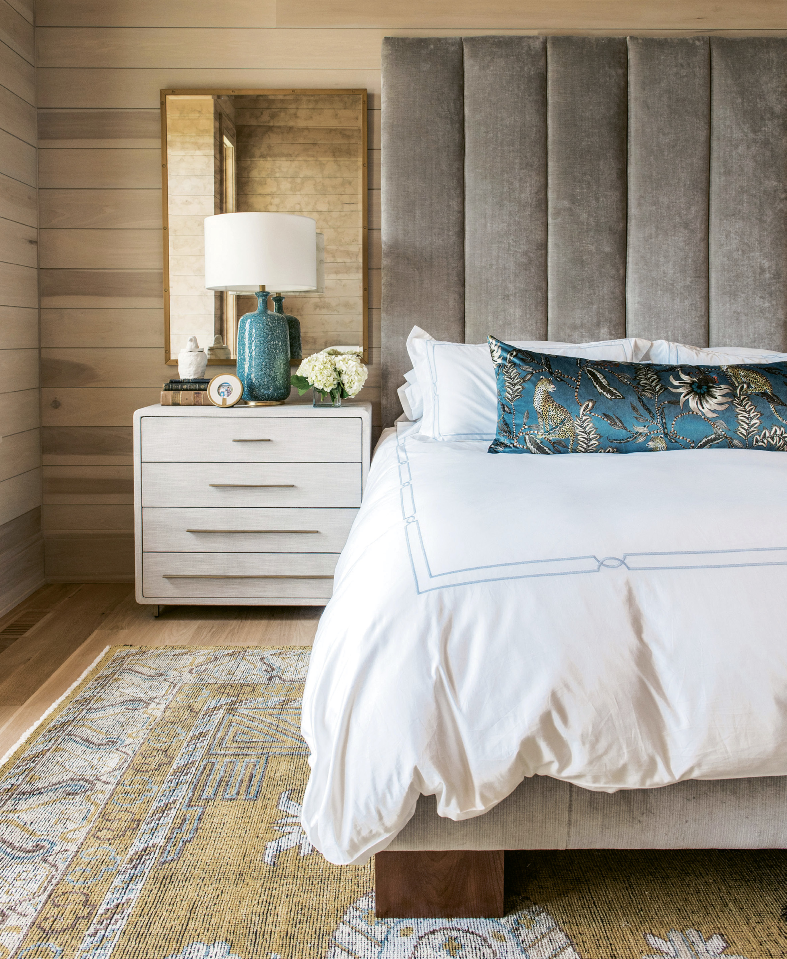In the couple’s bedroom, poplar-clad walls, velvet lumbar pillow (fabric from Ardmore Design), velvet headboard (custom designed by Erickson and upholstered by Powell’s Upholstery), and antiqued glass mirrors layer on the luxe.