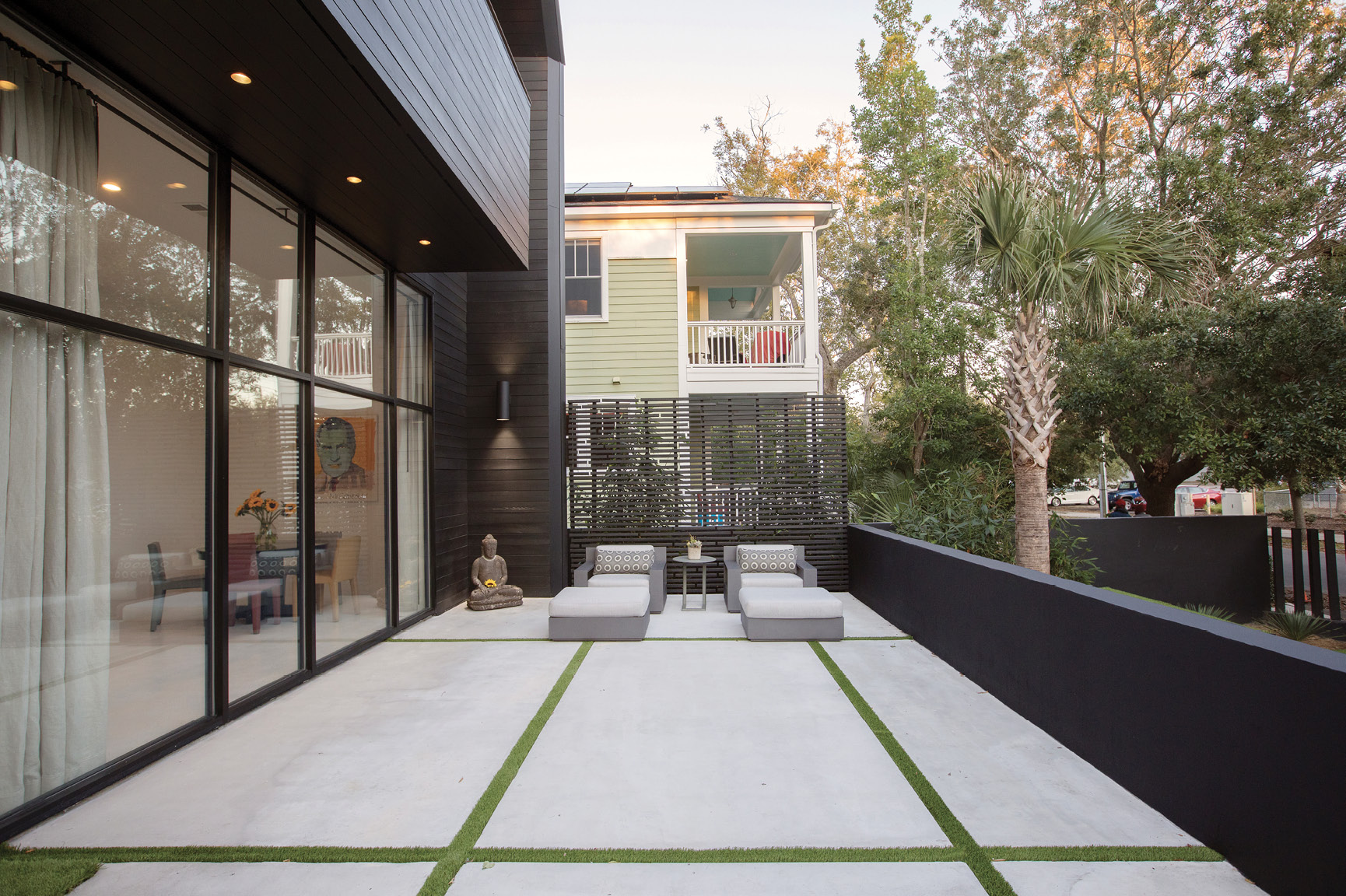 The front terrace strikes a contrast with the traditional porch behind it. Artificial turf between large concrete pavers soften the space, adorned by two Restoration Hardware lounge chairs.