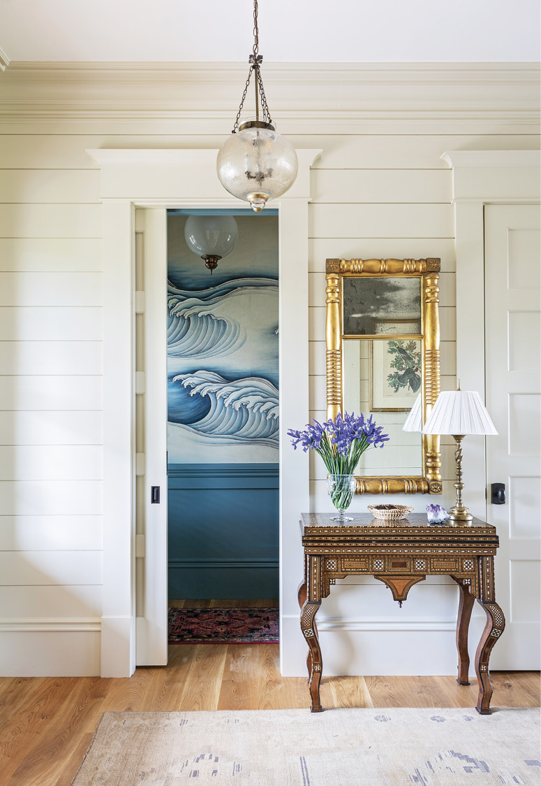 A WAVE THROUGH TIME: A bold blue and white hand-painted wallpaper from Gracie evokes the home’s nautical theme in the downstairs bathroom, while Martha’s grandfather’s exquisite 1920s Indian game table greets guest in the entryway.