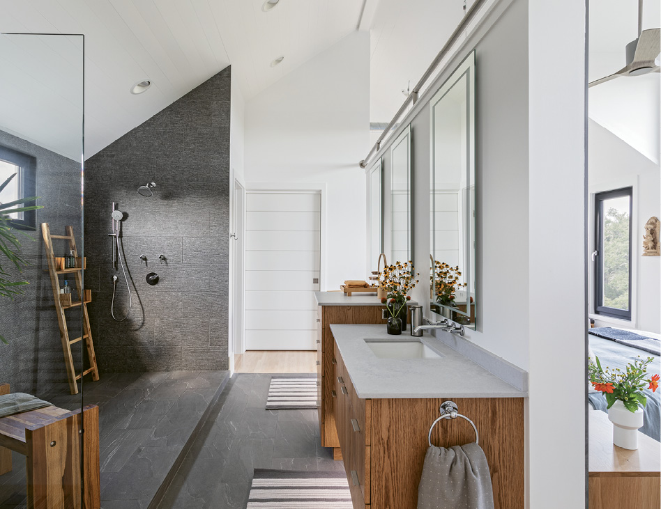 The unique open-plan master bathroom features a dramatic tiled shower and two floating vanities, supported by a freestanding wall that separates it from the bedroom. Touch-enabled LED lighting is built into the mirrors.