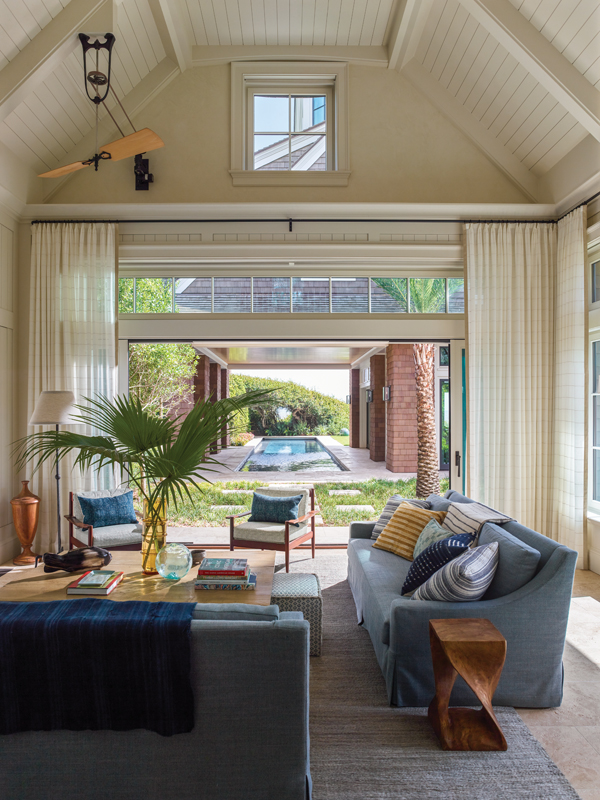 The separate pool house features a more casual living room with custom sofas upholstered in a blue Mariaflora outdoor fabric. A French twisted-wood side table from Lucca Antiques adds interest.