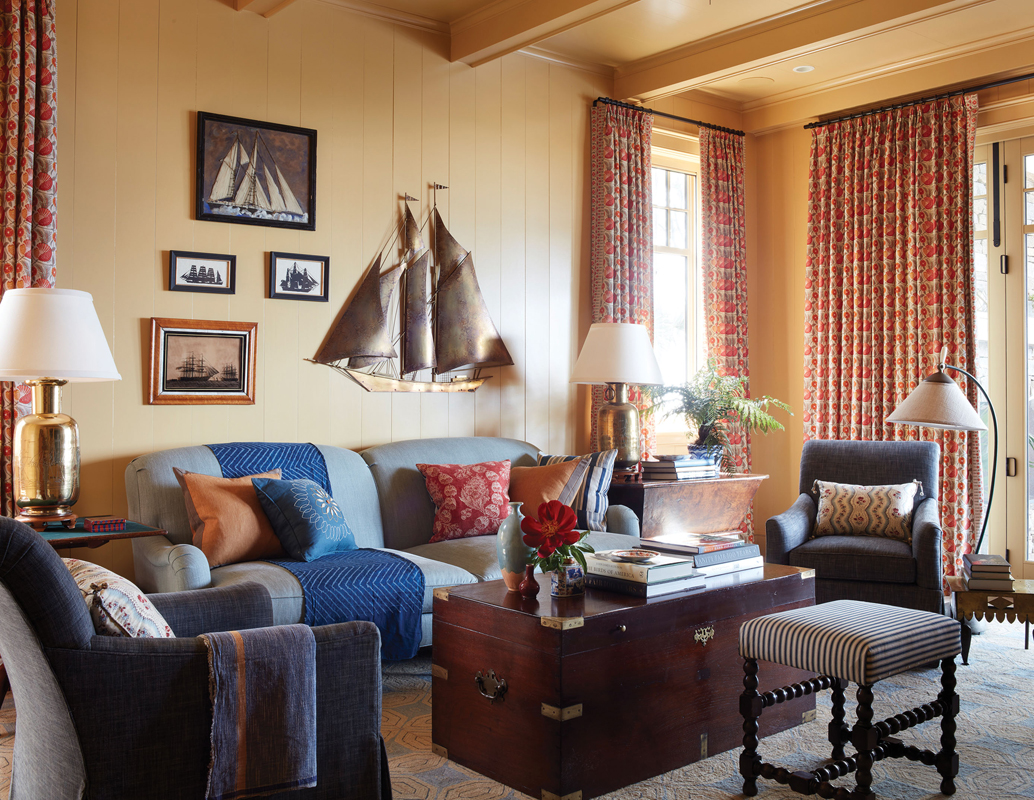 Get Cozy: The den’s warm palette and soft furnishings provide contrast with the rest of the open and bright downstairs living space. Walls painted in “Octagon Yellow” by Farrow &amp; Ball set the tone, where an overstuffed sofa from TCS Designs in North Carolina and Lee Jofa swivel chairs surround an antique trunk from Parc Monceau and chunky brass lamps from Fritz Porter shine.