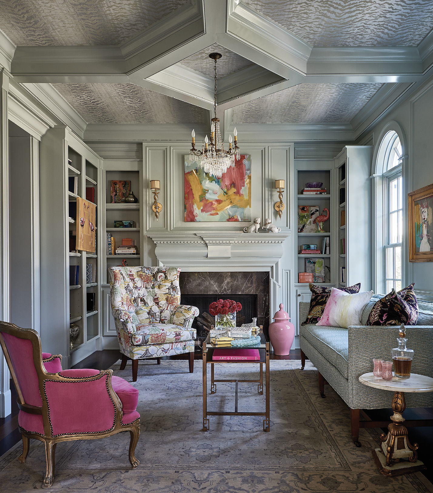 In the library, which was previously paneled in walnut, a pale mint paint (Farrow &amp; Ball “Cromarty No. 285”), Thibaut “Tiger Flock” wallpaper, pops of pink, and a crystal chandelier achieved the glamorous, New Orleans-inspired aesthetic the homeowner desired.