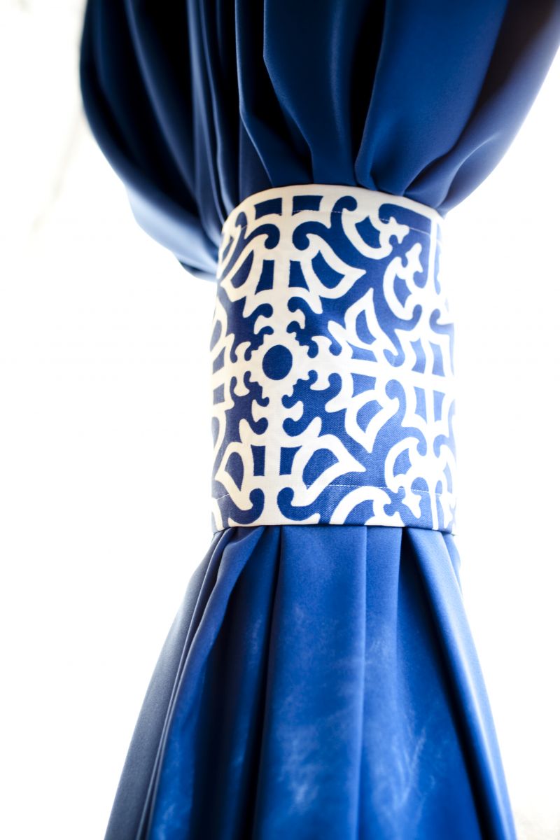HOLD BACK: Disguising the reception tent’s metal poles were blue velvet curtains held back by fabric featuring the invitation suite’s “lashar” motif.