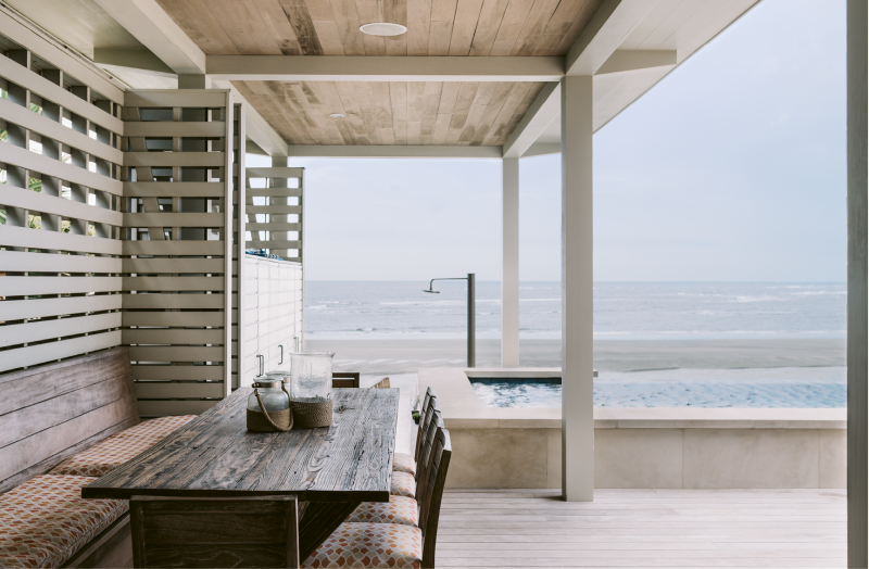 Elevated Entertaining - Dufford Young Architects nested an elevated deck of garapa and a zero-edge pool into the house, creating the family’s entertaining headquarters. A slatted wall offers privacy while allowing breezes to flow through the dining area with a large reclaimed wood table crafted by Landrum Tables.  Location: Isle of Palms  (owned by Suzanne Fine and Christian Salomone) Issue: September 2016, “Laid-back Luxe”  Photographer: Katie Charlotte