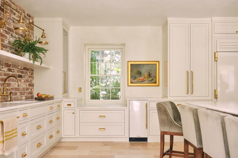 The large kitchen shines brightly courtesy of white cabinets, French limestone floors, and white marble countertops, with a matching backsplash above the cast iron-and-brass Italian Ilve range.