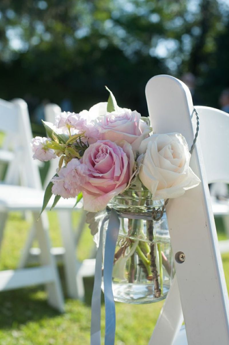 PINK ‘N’ BLUE: Blue ribbon-tied Mason jars filled with light pink roses, white roses, and carnations hung from chairs that lined the aisle.