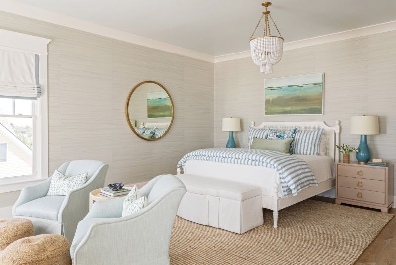 TOTALLY ZEN: Upholstered furnishings, grasscloth wallpaper, and a beachy palette make the primary bedroom a serene retreat. French doors lead out to a pergola-shaded private deck overlooking the ocean.