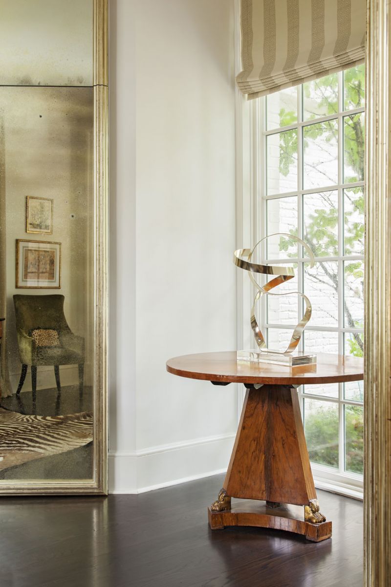 a Keen eye: Among the couple’s collection of artwork and antiques are the circa-1974 Ribbon Sculpture by Dan Murphy and Regency walnut center hall table purchased from Michael Bruno before he founded 1stdibs. The door to the bar is hidden by the full-length gilt-wood mirror, custom made by Bob Hines of R Squared Glass Artisans.