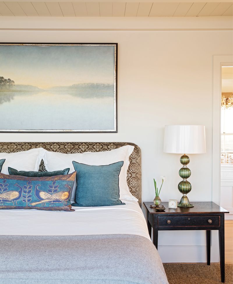 The Bright side: The primary bedroom suite is a study in refined elegance. A soothing landscape painting by local artist Mickey Williams resides above the headboard wrapped in Coleman Taylor “Gatsby Velvet.” Murano glass “Spheres” lamps with lacquered lampshades lined in gold rest atop heirloom bedside tables.
