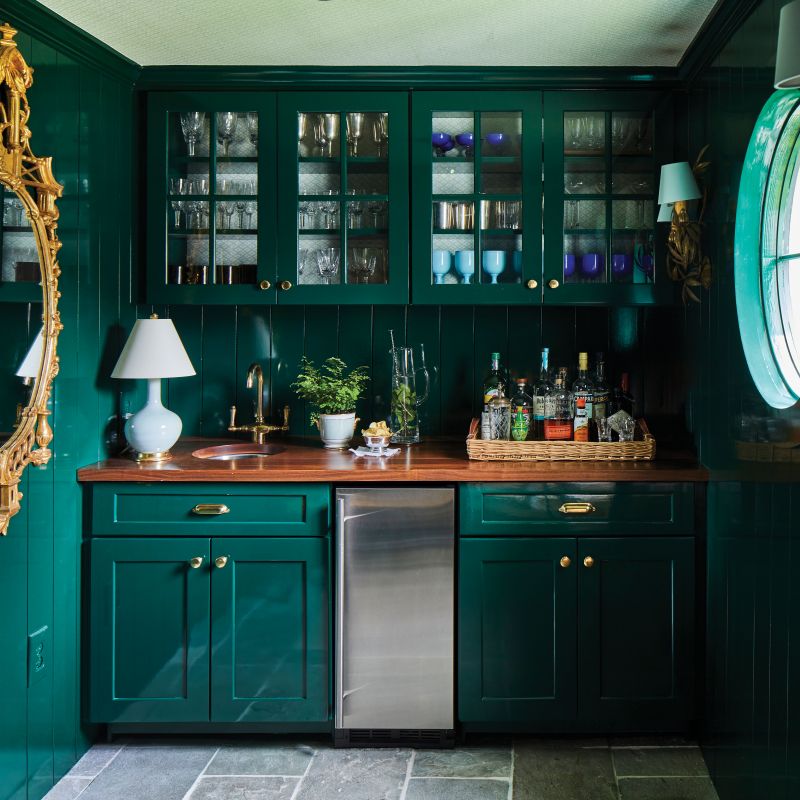 The lacquered bottle-green bar room—where family silver and crystal shine through custom cabinetry—is a handsome staging area for entertaining.