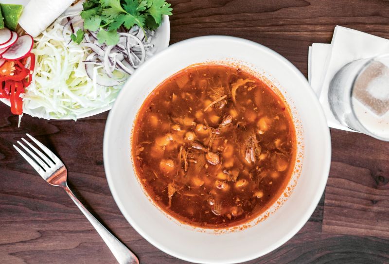 Pozole rojo, a hearty soup with pork shoulder and hominy, awaits fresh toppings.