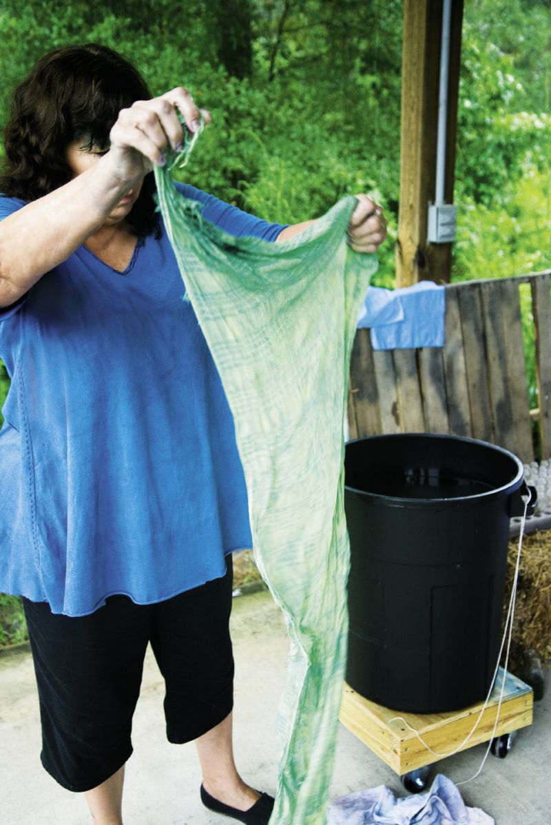 She squeezes out the excess water and pulls the linen out in a ball; contact with the air begins its transformation into a teal-green. Then she dips it in a solution of water, soda ash, and hydrogen peroxide to set the dye.