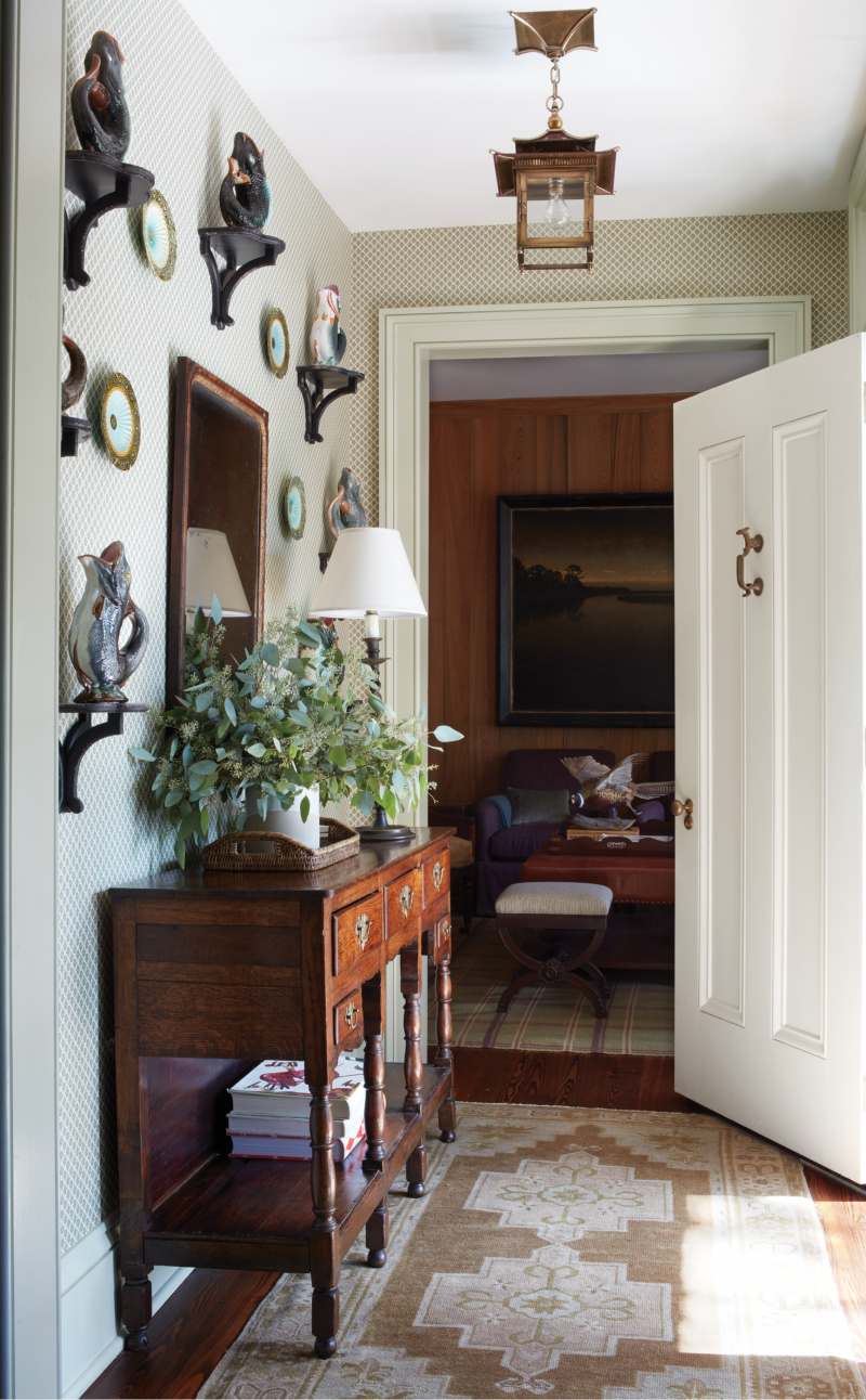 The family uses the rear entry, where the homeowner’s collection of traditional English stoneware “gluggle jugs” are artfully displayed above the 19th-century oak buffet. The space leads to the cypress-paneled den, with its stunning Lowcountry landscape by local artist Mickey Williams, to the right and the kitchen and breakfast room to the left.