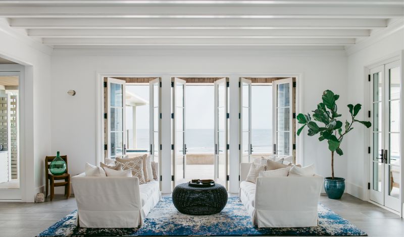 The living room is appointed with pieces in a coastal palette—such as a pair of neutral couches by Cisco Brothers and a custom blue and white rug by J.D. Staron—that don’t distract from views of the pool and the ocean beyond.