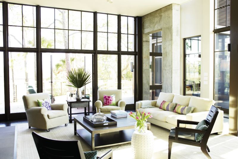 Neutral Territory: The wide-open living room is furnished simply with linen-upholstered sofa and chairs and a leather-top coffee table. It is enclosed on two sides by glass and opens to an ipé deck and screened porch.