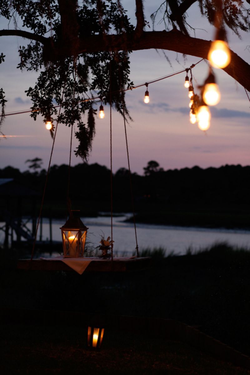 Marianne&#039;s husband strung strands of Edison bulbs across the property for the shoot. In lieu of traditional cocktail tables, they also hung pallets from trees and dressed them with linens and lanterns for a rustic alternative.