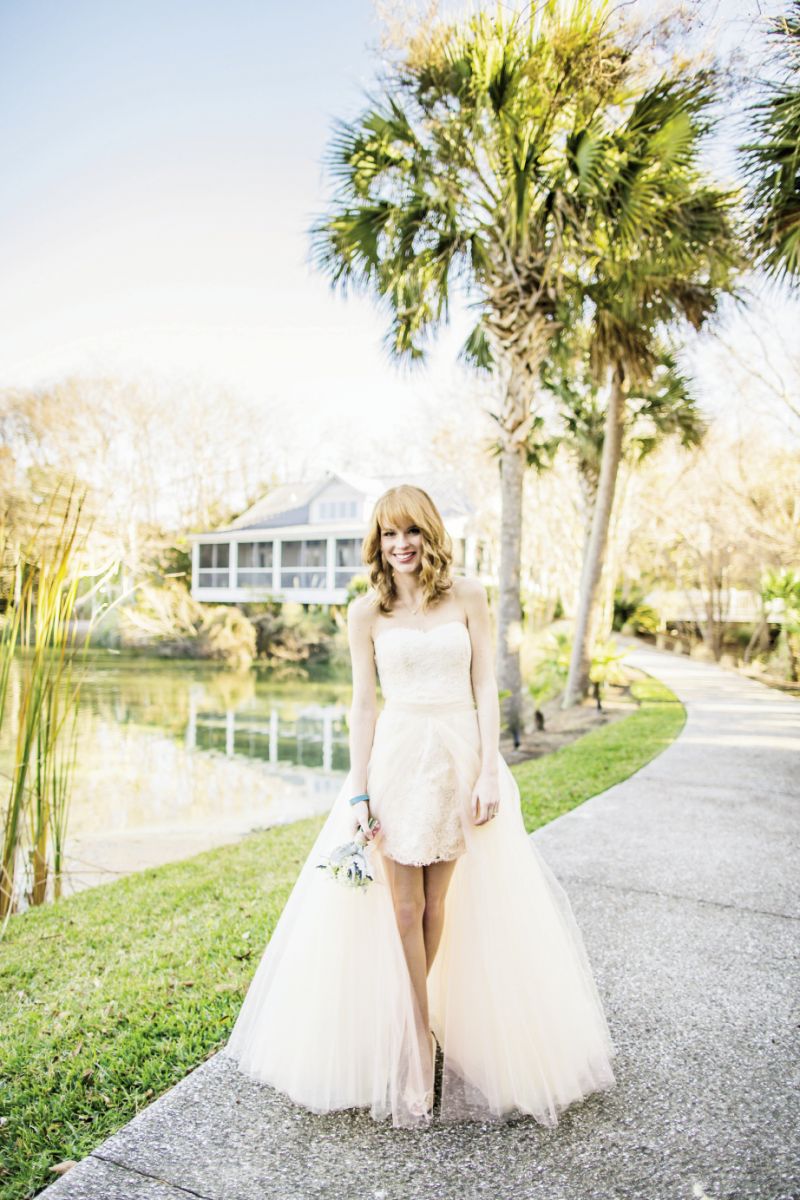 FRESH TAKE: Anne Barge’s “Sylvie” strapless Alençon lace dress with floor-length detachable pink tulle skirt from White on Daniel Island. Temple St. Clair’s 18K yellow gold pendant necklace from Croghan’s Jewel Box. Marco Bicego’s 18K yellow gold ring with Jaipur topaz and diamonds from REEDS Jewelers. Leighelena turquoise stingray bracelet from Out of Hand. Nina’s “Electra” gold satin d’Orsay pumps from Bella Bridesmaid. Bouquet by Tiger Lily.