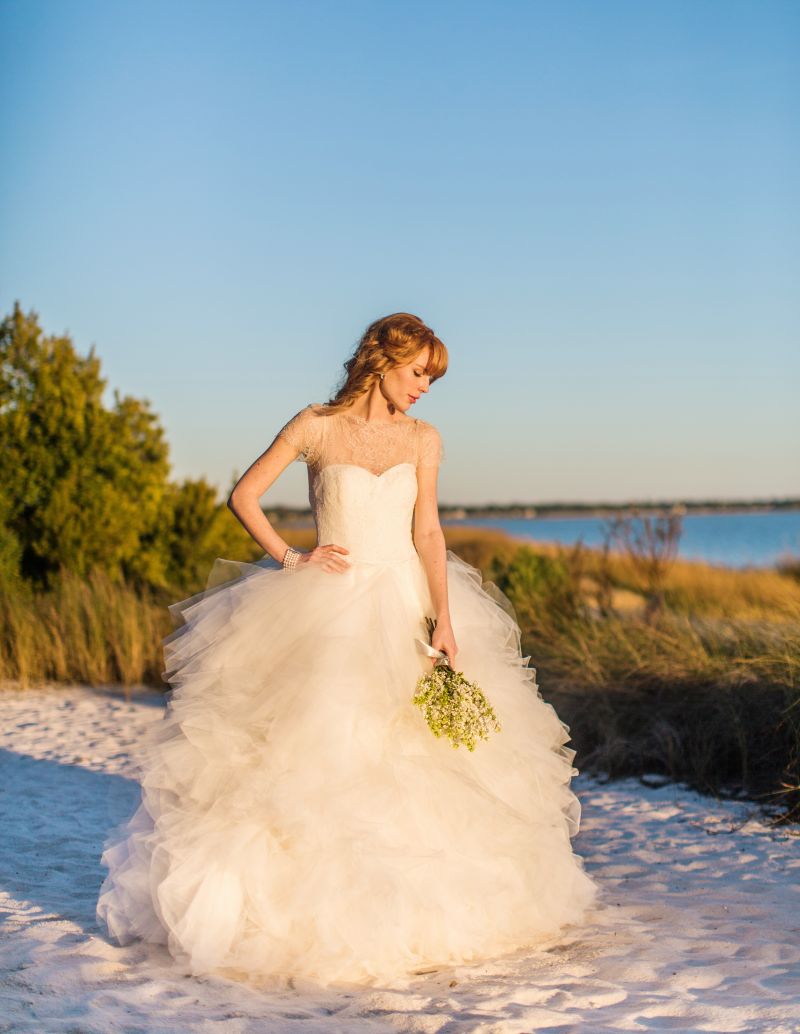 BEACH BABE: Marchesa’s “Theodora” lace bodice and layered tulle ball gown from White on Daniel Island. Matthew Campbell Laurenza’s sterling silver, quartz, and rhodium earrings from Paulo Geiss. Cultured pearl bracelet and 18K white gold, emerald, and diamond ring, both from Croghan’s Jewel Box.