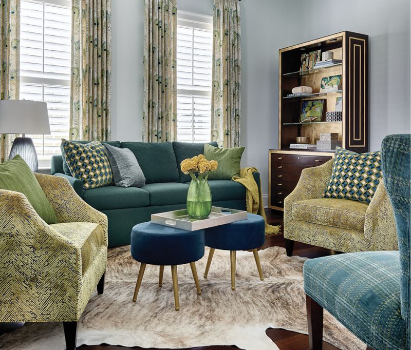 Two Baker “Butterfield Barrel Chairs” covered in a citrus-green fabric provide the focal point for the striking home office. Peacock feather drapes, a cowhide rug, and two velvet footstools complete the luxe look.